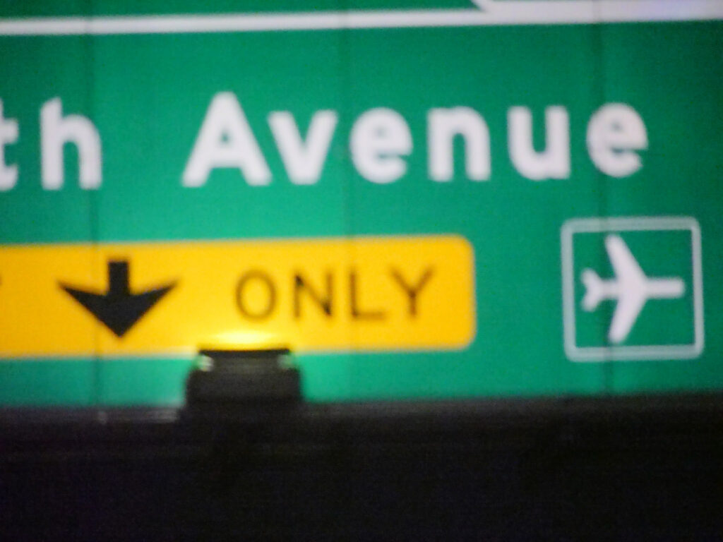 A nighttime highway sign points toward Seventh Avenue and the airport.