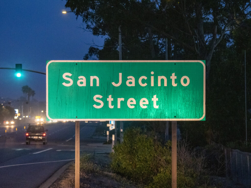 A green street sign for San Jacinto Street photographed at night.