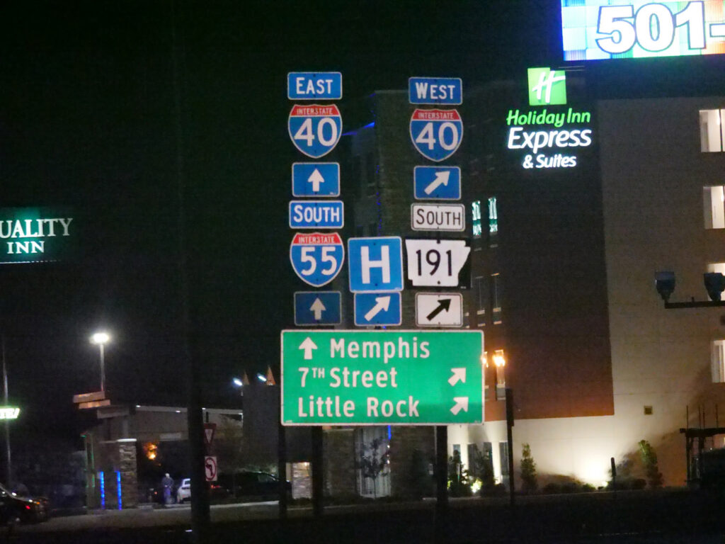 A dense stack of interstate and business-route signs photographed at night.