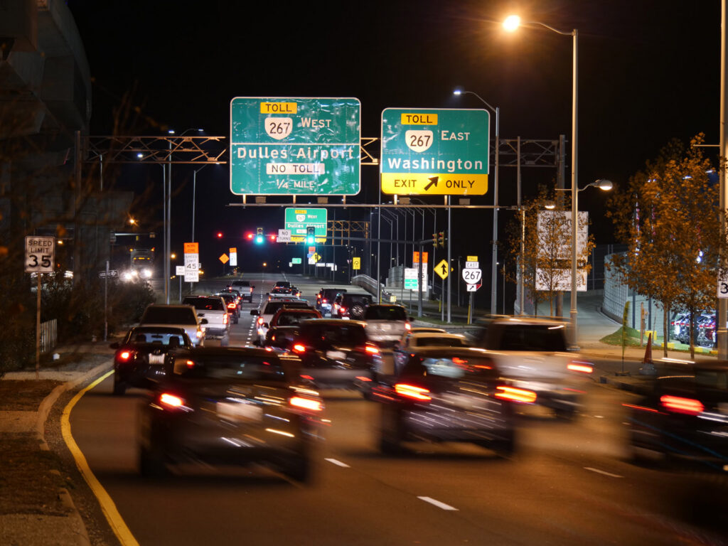 Overhead freeway signs guide nighttime traffic through an urban roadway.