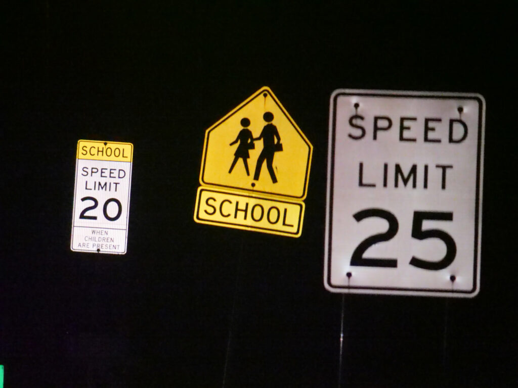 School zone and speed limit signs photographed at night along a local road.