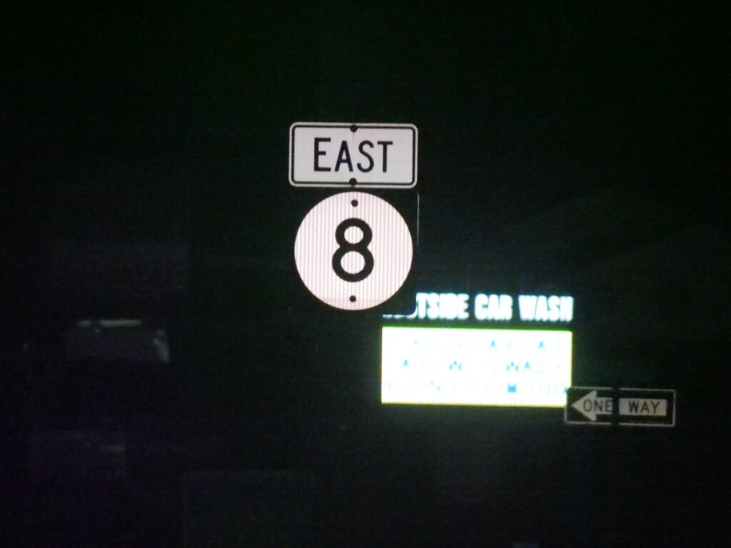 A U.S. Route 8 shield and roadside guide sign photographed at night.