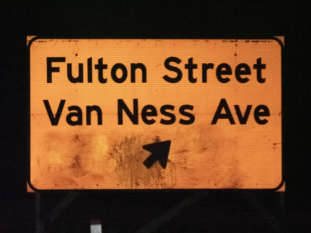A yellow guide sign directs traffic toward Fulton Street and Van Ness Avenue.