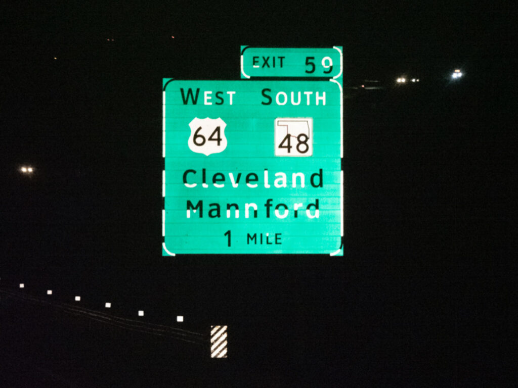 A green highway guide sign lists Cleveland and Hartford destinations at night.
