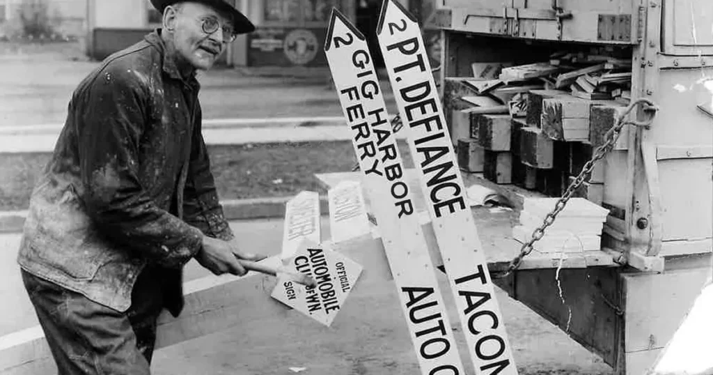 This image shows an early 20th-century worker in Washington state preparing American Automobile Association (AAA) directional signs for installation, pointing toward local landmarks such as Gig Harbor, Pt. Defiance, and Tacoma. The AAA Washington club began installing these recognizable white arrow signs in 1906 to help early motorists navigate, and by 1920 thousands of them stood across Western Washington, marking directions, distances, and speed limits. — Seattle Sun Times