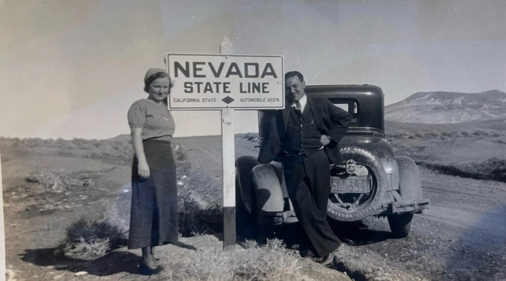People standing beside a Nevada state line sign next to an automobile.